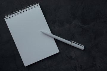 Clean notepad and pen on dark background with texture. Concept for education or business with space for text. Notebook with white paper for writing notes, top view.