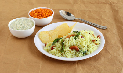 Lemon rice, a traditional, popular, and homemade south Indian vegetarian breakfast on a plate with potato chips, and coconut chutney as a side dish.
