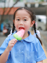 Adorable little Asian child girl in school uniform eating ice-cream in the park.