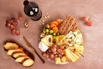 Cheese set on a plate laid out on a beige background. Different types of cheeses: Camembert, Parmesan, blue cheese, olives, honey, grapes.