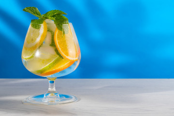 Refreshing cocktail with orange lemon lime mint and ice on a bright blue background
