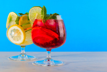 Two refreshing cocktails with orange lemon lime mint and ice on a bright blue background