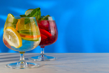 Two refreshing cocktails with orange lemon lime mint and ice on a bright blue background