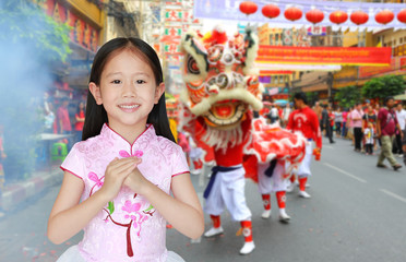Happy little Asian child girl wearing pink traditional cheongsam dress with greeting gesture celebration for Chinese New Year on chinese background.