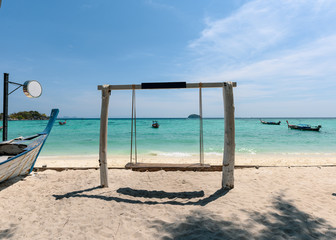 Wooden swing on the beach with long-tail boat in tropical sea