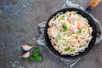 Italian pasta spaghetti in a creamy sauce with shrimp in a frying pan, top view