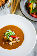 Mexican lunch, gazpacho soup with crackers and hot peppers in a white plate. tomato soup with vegetables. mexican soup. Puree soup tomato with croutons. Diet menu. tomato soup in a white plate