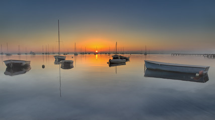 Boote liegen friedlich im Wasser während im Hintergrund die Sonne aufgeht