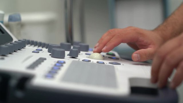 Close up hands of doctor presses buttons and works on ultrasound device. 