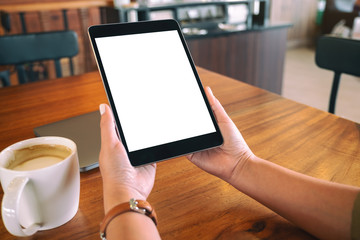 Mockup image of hands holding black tablet pc with blank white screen with coffee cup on wooden table