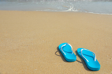 Fototapeta na wymiar Tropical summer vacation concept. Flipflops on a sandy ocean beach. Blue beach shoes on the sandy seashore.
