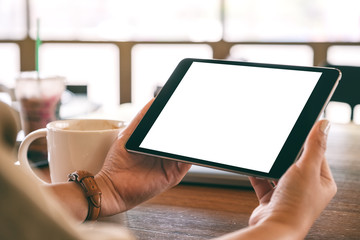 Mockup image of hands holding black tablet pc with blank white screen horizontally with coffee cup on wooden table
