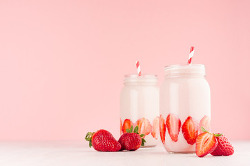 Set of two fresh cold milkshake in hipster jars with cut ripe berries, striped straws in elegance pink kitchen interior, copy space, closeup.