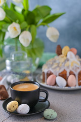 Obraz na płótnie Canvas Fragrant cup of coffee and Easter orthodox sweet bread, kulich and colorful quail eggs with willow branches. Holidays breakfast concept with copy space. Set for the holiday and a bouquet of tulips.