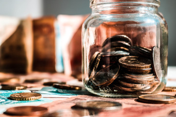 Glass jar with coins on the floor of banknotes. Blurred banknotes on the background.
