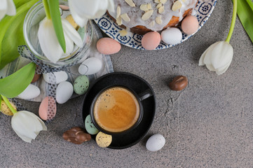 A cup of aromatic coffee with froth over a gray background, white tulips and chocolates for Easter. Copy space, flat lay.