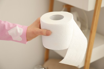 Young woman holding soft toilet paper from shelf in restroom
