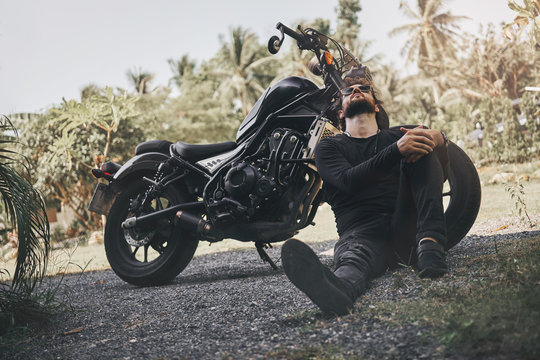 Handsome biker man in black wear sit near classic style cafe racer motorcycle. custom made motorcycle