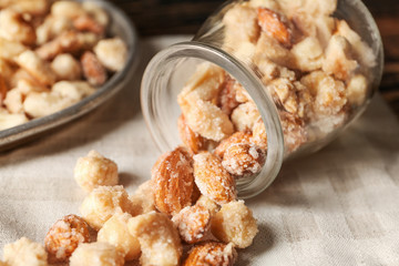 Jar with tasty sugared nuts on table