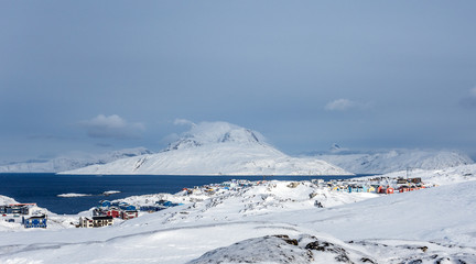 Inuit houses and cottages scattered across snow tundra landscape in residential suburb of Nuuk city with fjord and mountains in the background, Greenland