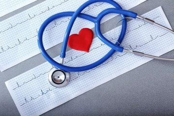 Stethoscope with cardiograms on grey background