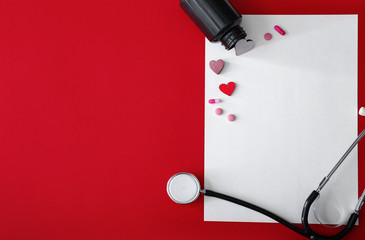 Stethoscope with sheet of paper and pills on color background