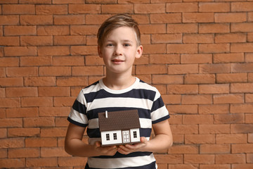 Little boy with model of house on brick background. Concept of earthquake