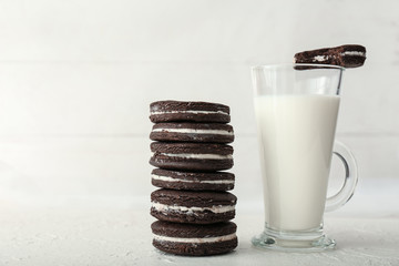 Stack of tasty chocolate cookies with glass cup of milk on light background