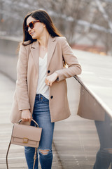 Beautiful girl in a park. Stylish brunette in a brown jacket. Lady in a sunglasses