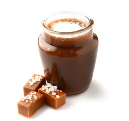 Jar of tasty salted caramel with candies on white background