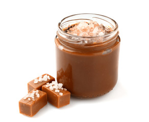 Jar of tasty salted caramel with candies on white background