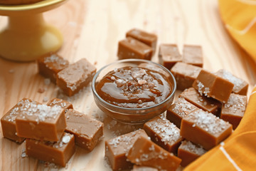 Bowl of tasty salted caramel with candies on wooden table