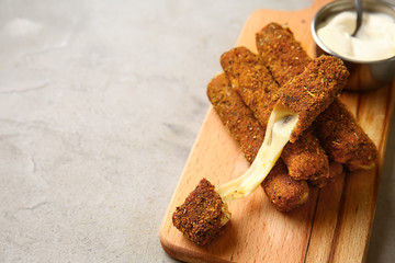 Wooden board with tasty mozzarella sticks and sauce on grey table