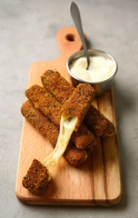 Wooden board with tasty mozzarella sticks and sauce on grey table