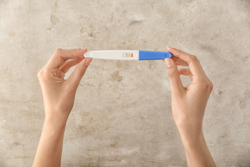 Female hands with pregnancy test on grey background