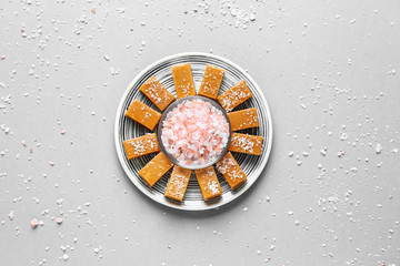 Plate with tasty candies and salt on grey background
