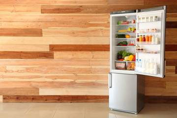 Open fridge full of food near wooden wall