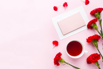 Red-pink objects. Cup of tea, carnation flowers Notepad for text on pastel pink background. Copy space. Top view Flat lay