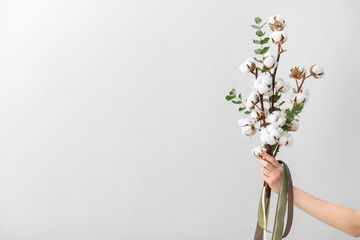 Female hand holding floral composition with cotton flowers on light background