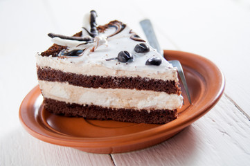 Delicious cake. Layers of delicate cream and chocolate sponge cake. On a plate, on a white wooden background. Dessert for the holiday