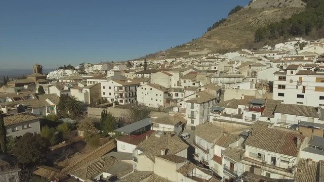 Low aerial shot of sightly stacked white buildings in Cazorla city with olive groves at the distance