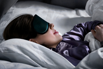 Young woman with sleep mask in bed at night