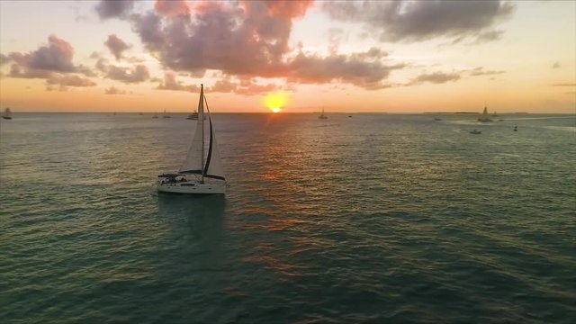 Sailboat floats as the sun sets while a drone orbit's around the boat in crisp 4K resolution.