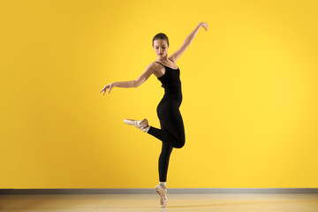 Beautiful young ballerina against color wall