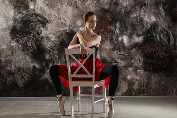Beautiful young ballerina sitting on chair against grunge wall