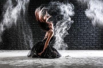 Obraz na płótnie Canvas Beautiful young ballerina dancing with powder against dark wall