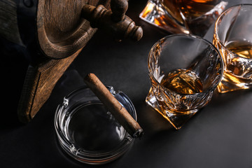 Glasses of cold whiskey with cigar and barrel on dark background