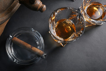 Glasses of cold whiskey with cigar and barrel on dark background