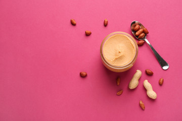 Jar with peanut butter on color background