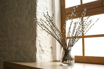 Glass vase with willow branches on wooden windowsill at home